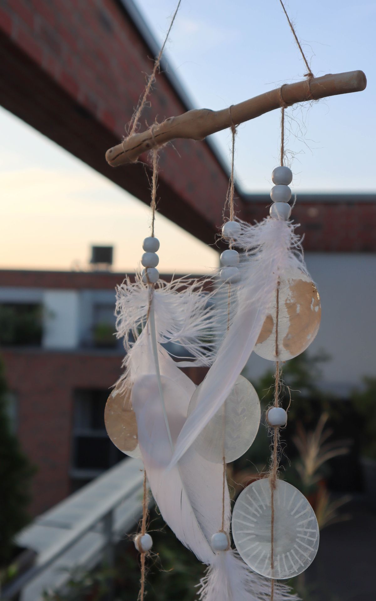 Windspiel basteln aus Naturmaterialien: Ich zeige dir, wie du ein bezauberndes Boho-Windspiel mit Muschelscheiben, Federn und Holzperlen selbst gestalten kannst. Die perfekte DIY-Idee für eine individuelle Garten- oder Hochzeitsdekoration.